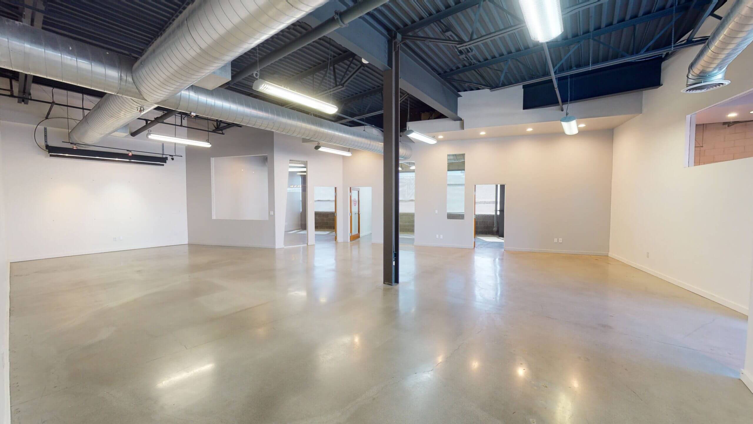 Spacious empty commercial interior with polished concrete floors and exposed ceiling.
