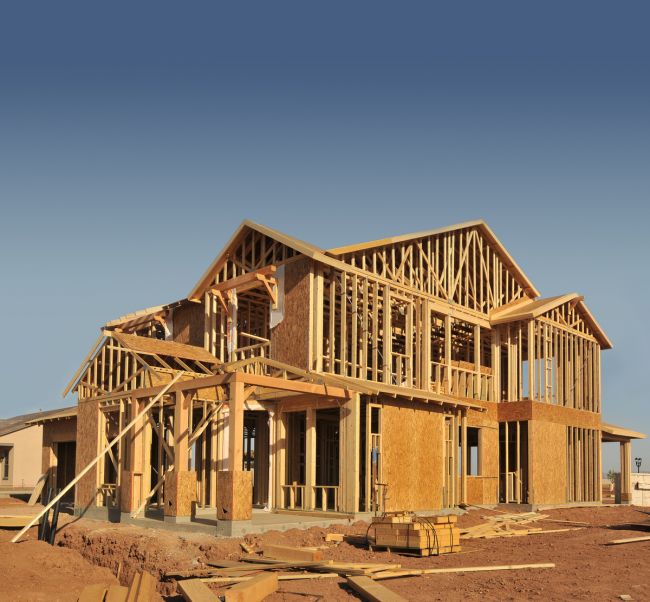 Wooden framework of a two-story house under construction on a clear day.